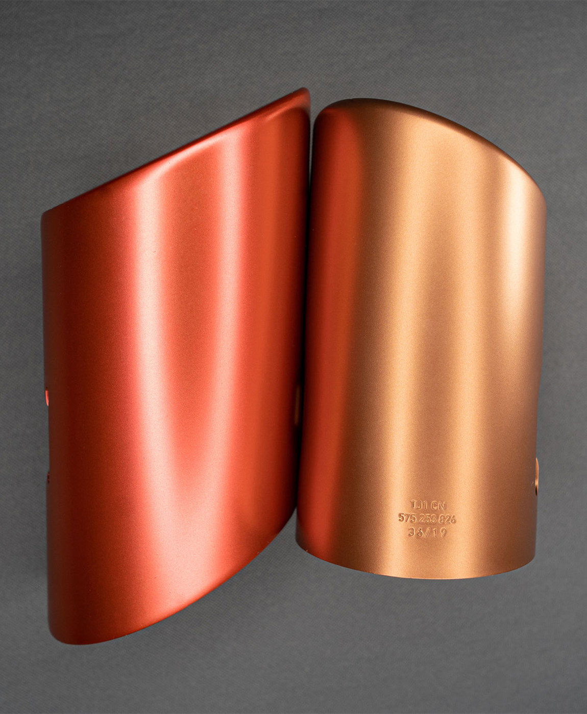 Zwei farblich abgestimmte Abgas-Endrohre mit hochwertiger Metallbeschichtung in Kupfer- und Bronzeton, liegend auf einem strukturierten, dunklen Untergrund.