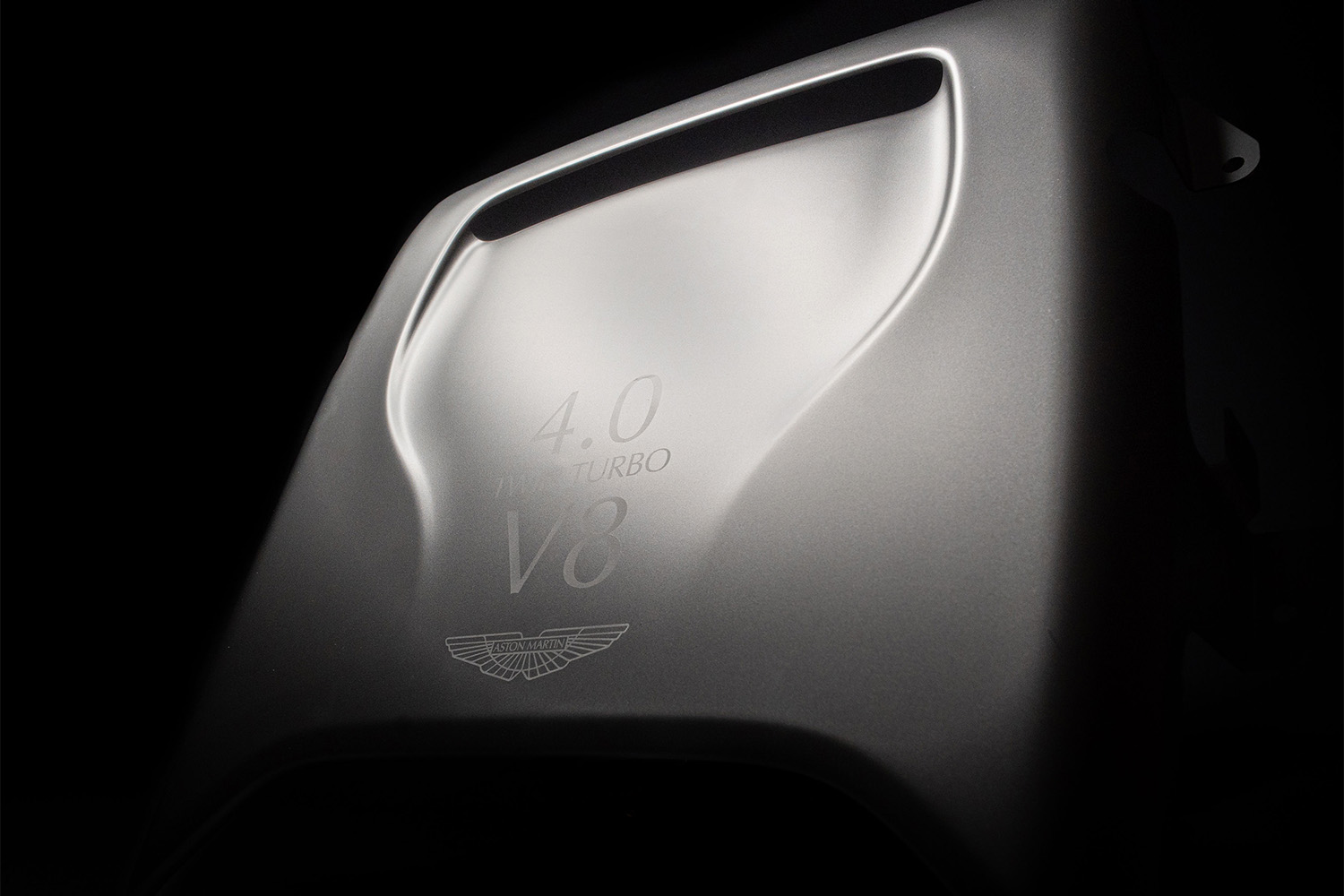 Elegante Motorabdeckung eines Aston Martin mit matter Metallic-Oberfläche und eingeprägter „4.0 V8 Twin Turbo“-Beschriftung.