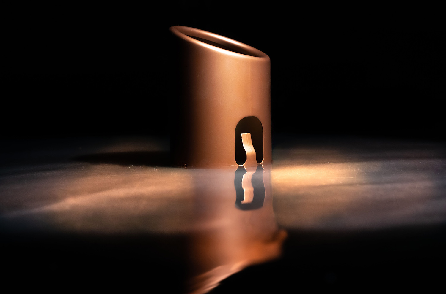 High-quality coated metal component in warm bronze look with atmospheric light reflection on dark background.